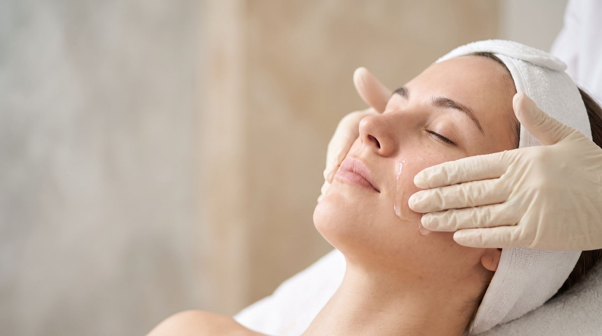 A clinician's gloved hands smoothing serum onto a relaxed woman's cheek