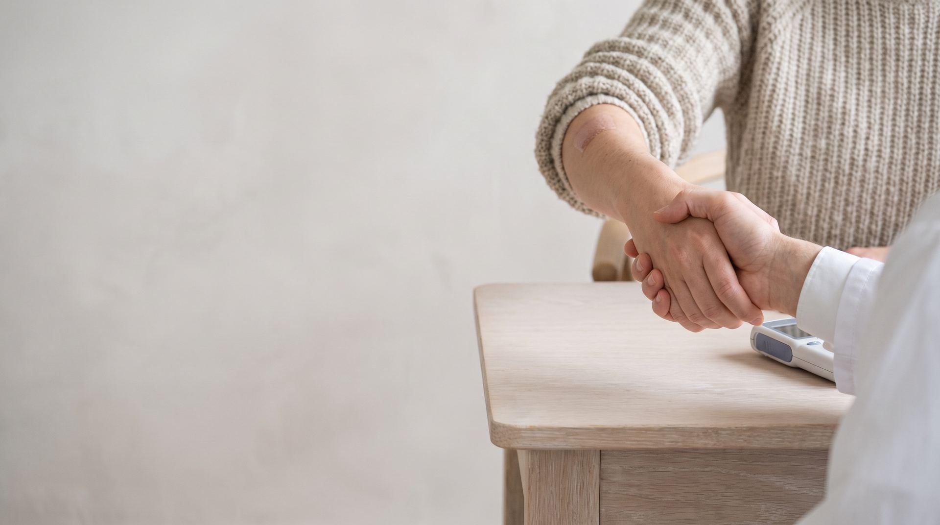 A doctor and a patient shaking hands across a desk
