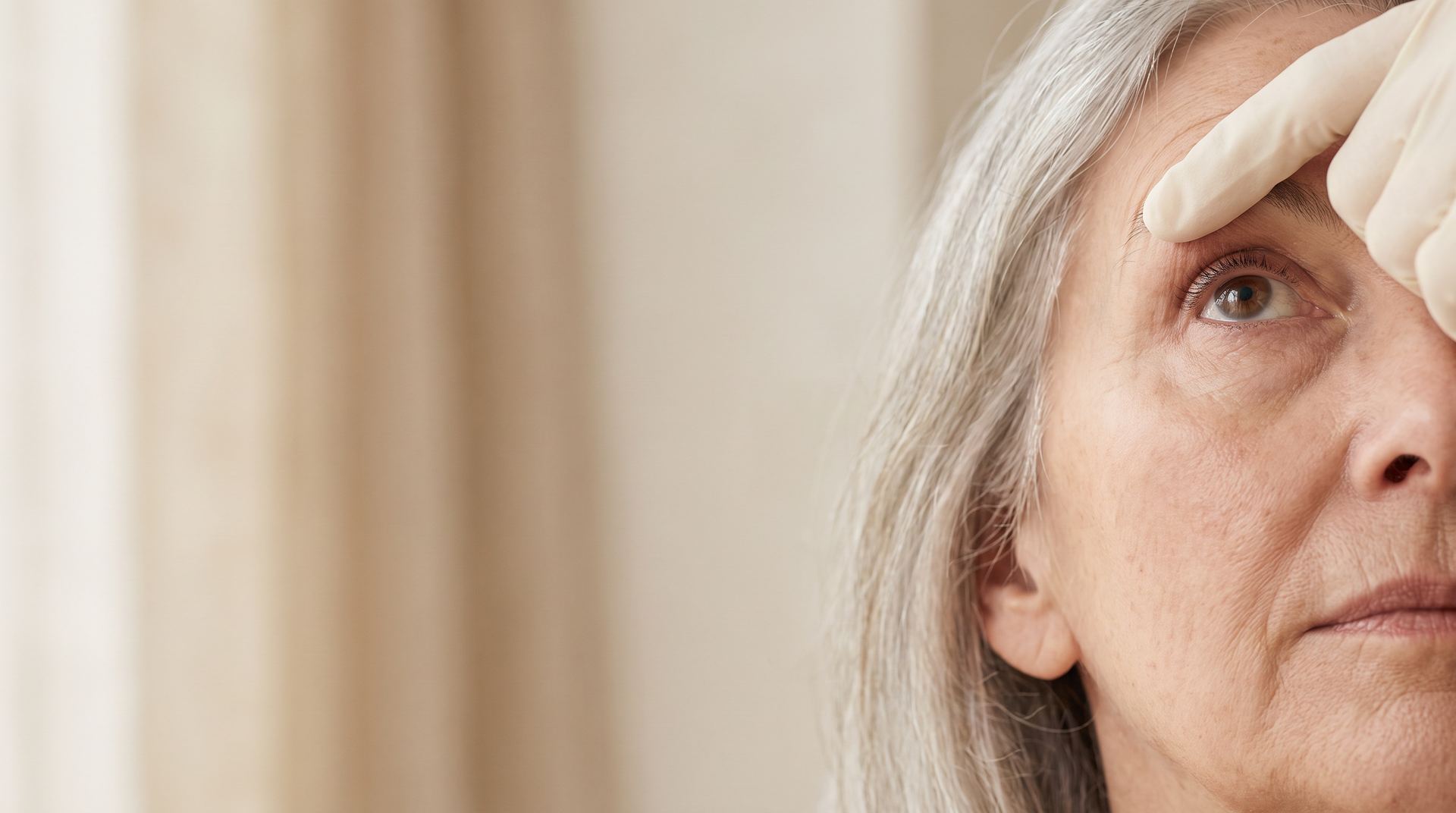 A clinician's gloved fingertip gently lifting a woman's upper eyelid