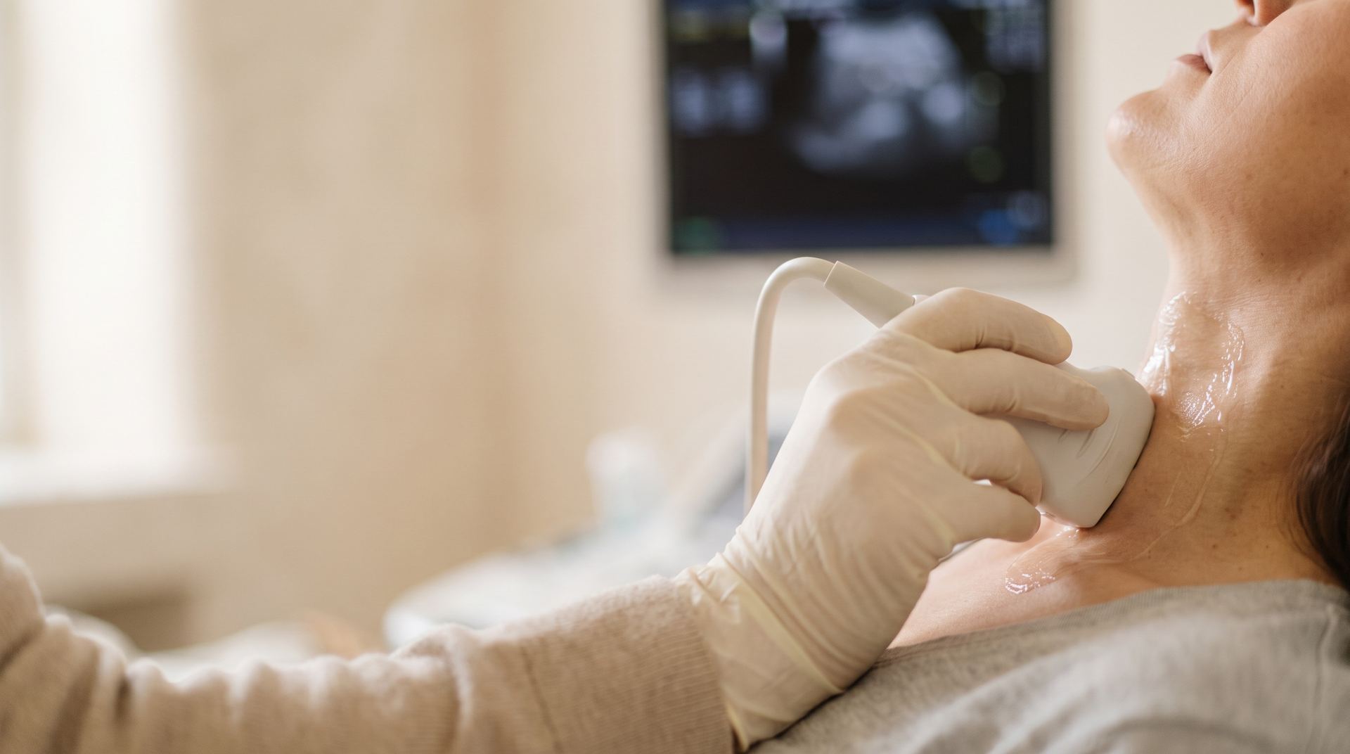 A gloved hand holding an ultrasound probe against a woman's neck