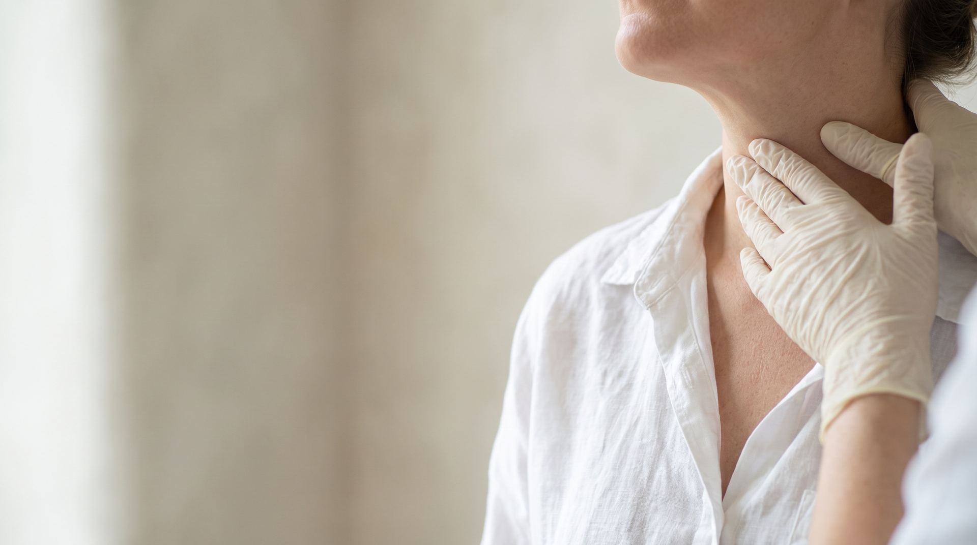 A clinician's gloved fingertips examining the front of a woman's neck