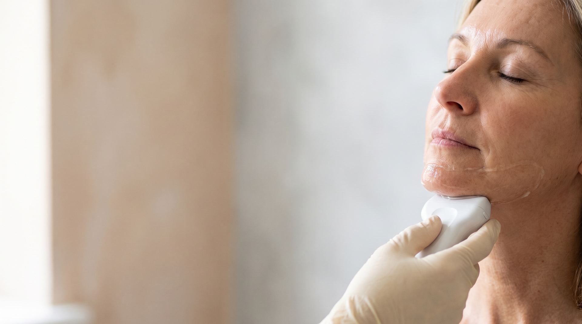 A gloved hand holding an ultrasound handpiece under a relaxed woman's jaw