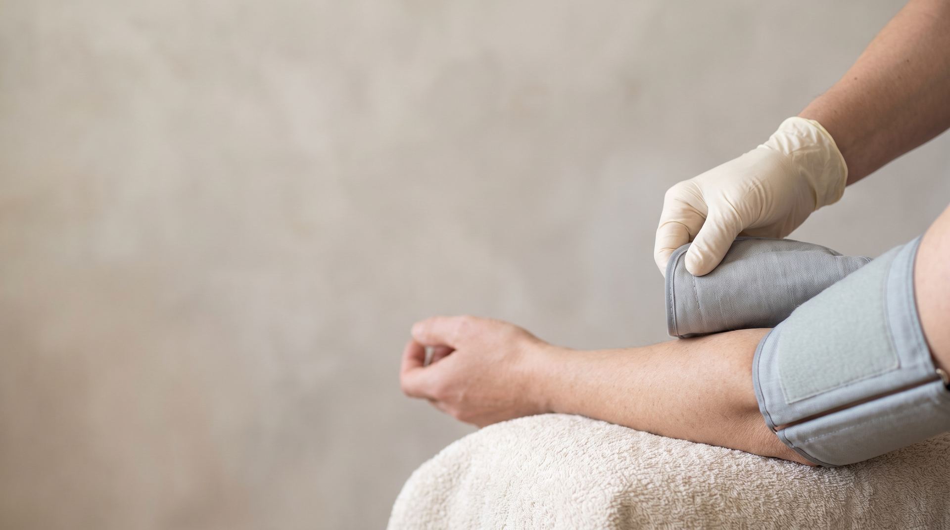 A clinician's gloved hand fitting a blood pressure cuff to a patient's arm