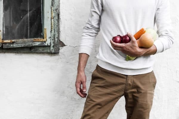 Sporting a white sweater and brown pants, an individual holds fresh vegetables like corn and onions against a white wall. Taking care of your gut health with these wholesome foods can bolster your immune system, fortifying it in the fight against coronavirus. - Meyer Clinic