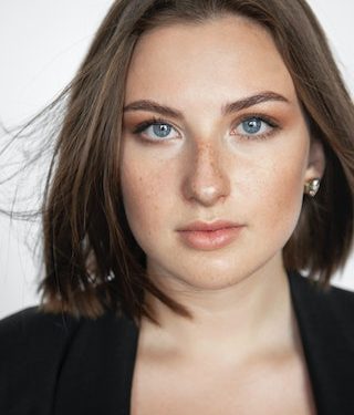 A person with short brown hair and blue eyes wearing a black top, facing the camera against a plain background, radiates confidence under LED Phototherapy lighting. - Meyer Clinic