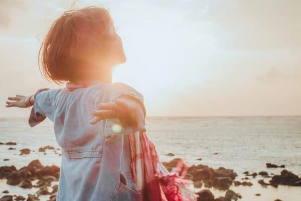 Person with outstretched arms facing the sun at a rocky beach during sunset, embracing nature’s serene beauty—a perfect moment to boost your oestrogen levels naturally. - Meyer Clinic