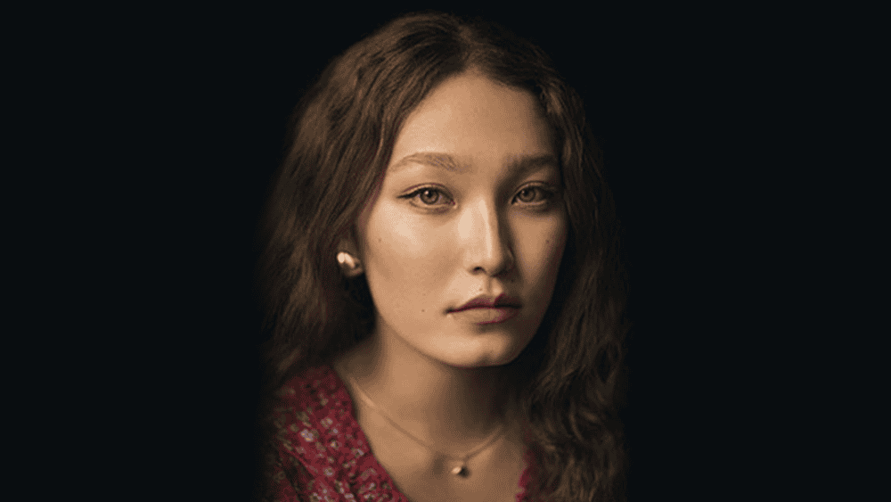 A woman with long, wavy hair wearing a red top looks directly at the camera against a dark background, showcasing the radiant effects of non-surgical skin tightening. - Meyer Clinic