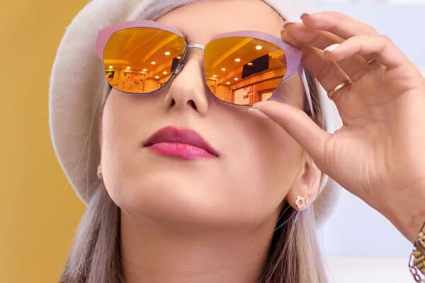 A woman wearing cat-eye sunglasses adjusts them while looking up. With pink lipstick and a light beret, her hair is partially visible, hinting at the glow one might achieve from a superficial chemical peel. - Meyer Clinic