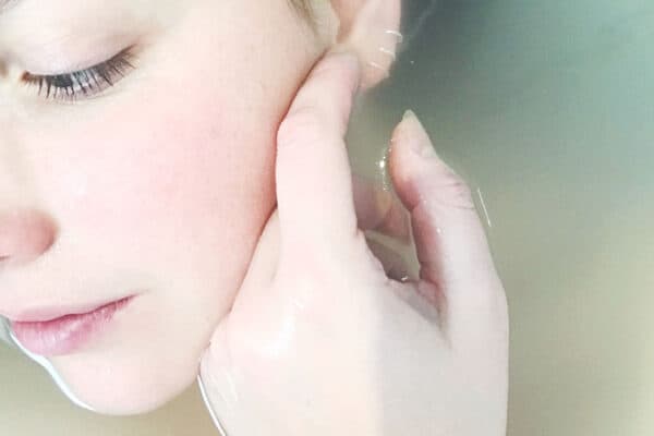 Close-up of a person touching their ear while submerged in water, eyes closed, and face partially visible, reflecting a serene moment of relief from blemishes after effective laser treatment. - Meyer Clinic