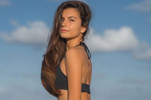 Person with long hair wearing a black swimsuit, enjoying the clear blue sky and fluffy clouds, perhaps contemplating laser hair removal for a smoother look. - Meyer Clinic