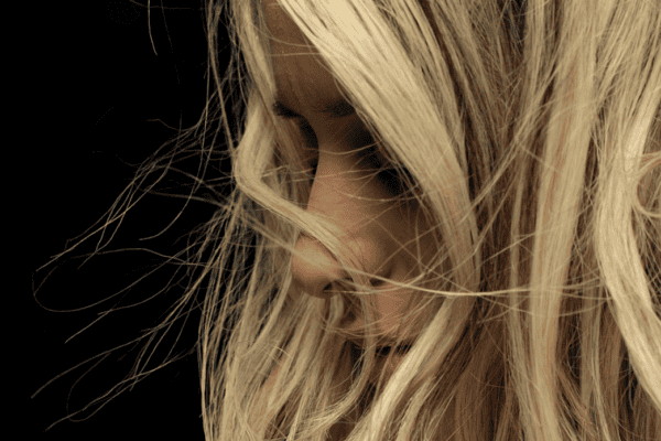 A close-up of a person with long, blonde hair, partially obscuring their face against a dark background—a reminder of the transformative magic of hair rejuvenation at the Meyer Clinic. - Meyer Clinic