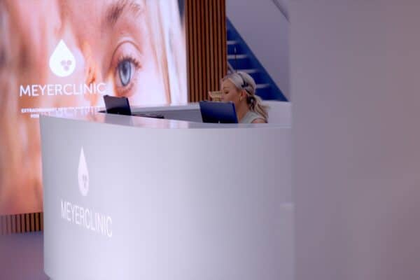 At the reception desk of Meyer Clinic, a team member works diligently on a computer, while a large screen behind them displays the clinics logo and an eye image, showcasing the practices commitment to exceptional care. - Meyer Clinic