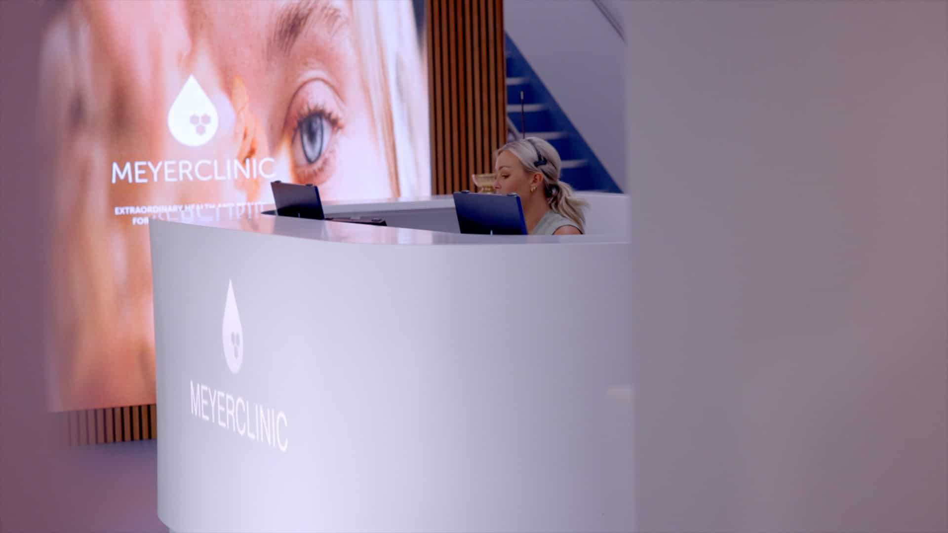 At the reception desk of Meyer Clinic, a team member works diligently on a computer, while a large screen behind them displays the clinics logo and an eye image, showcasing the practices commitment to exceptional care. - Meyer Clinic