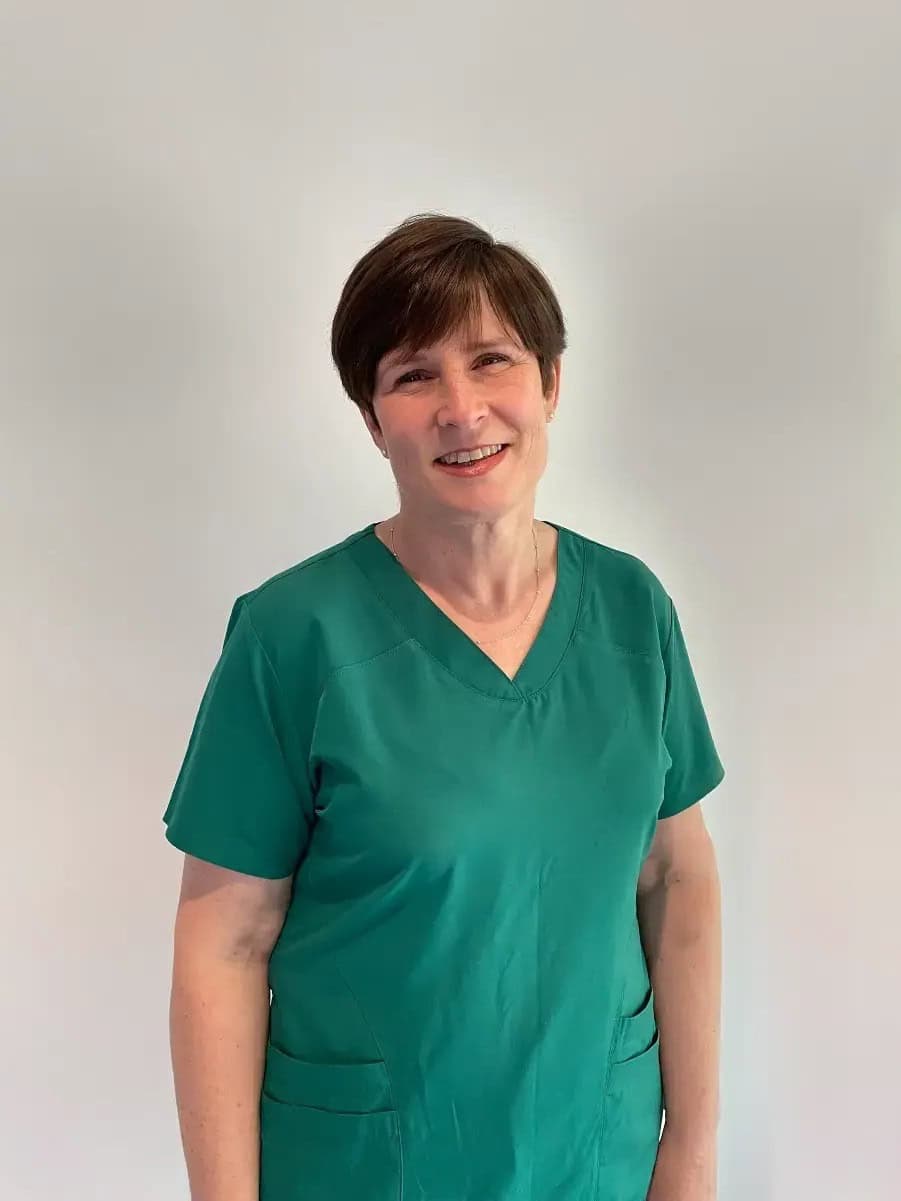 A person wearing green medical scrubs stands against a plain light background, smiling at the camera. - Meyer Clinic